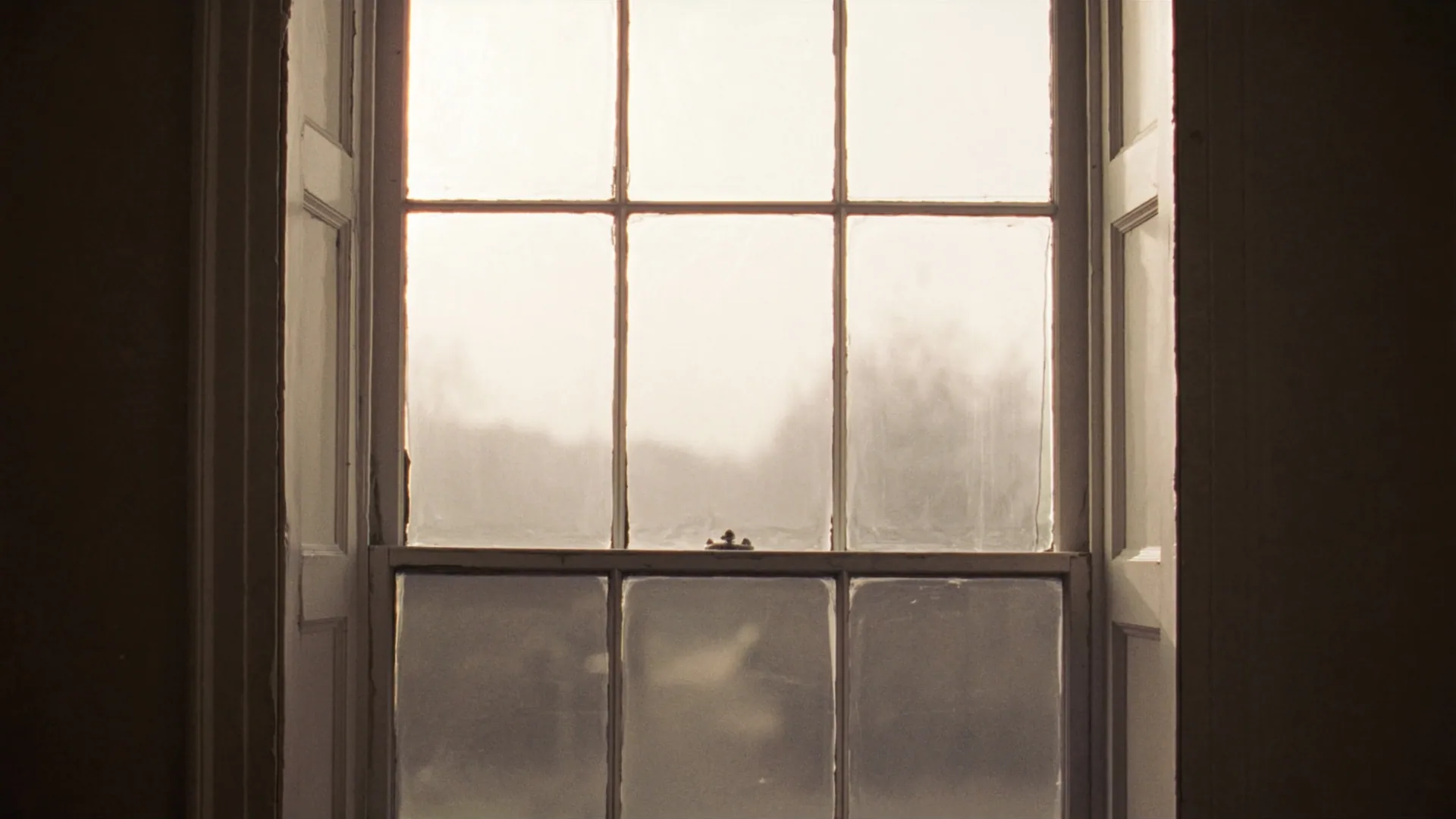 Soft morning light pouring through a Victorian sash window, viewed from inside an empty period room